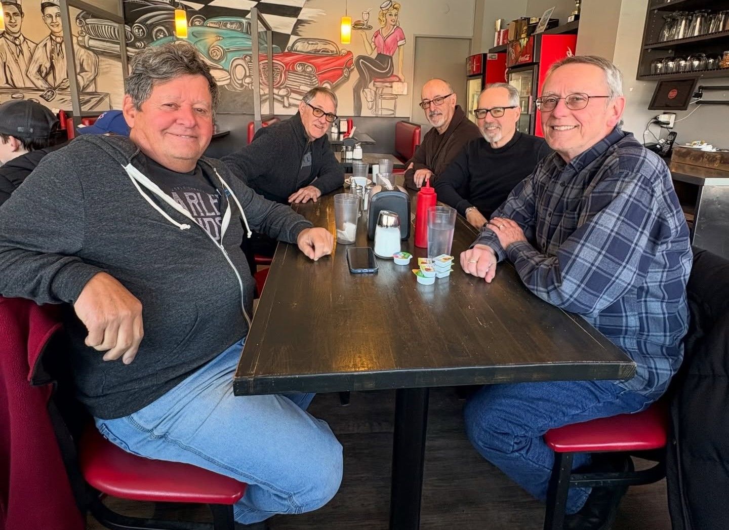 A group of 5 men sit and smile at a diner table